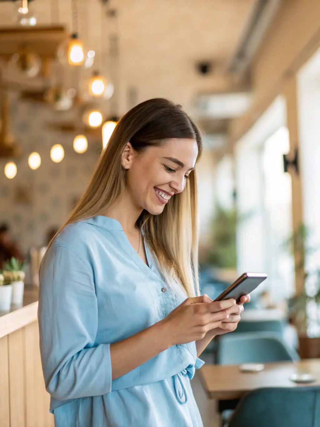 A person using a budgeting app on their phone while sitting at a kitchen table with a laptop and family photos in the background, conveying a sense of calm and control over finances.
